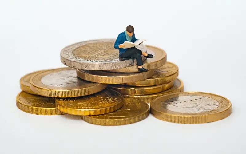 A little man sits on a pile of Euros reading. He is researching how he can best monetize his Tickaroo Live Blogs. 